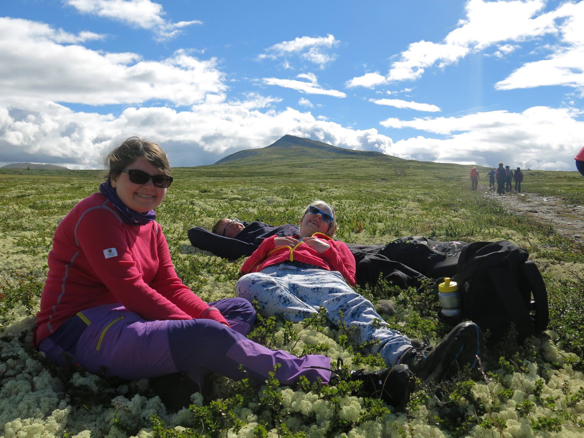 Fjellcamp 2017 17 Bildet viser en gruppe unge voksne som går på tur mot en fjelltopp, mens tre stykker hviler seg litt på veien